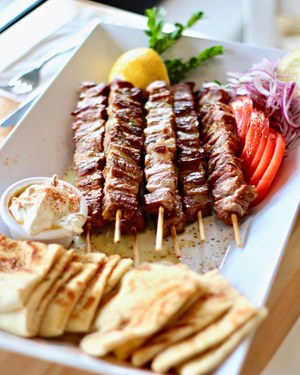 Grilled pork souvlaki skewers with toasted pita, tomato, red onion, and tzatziki